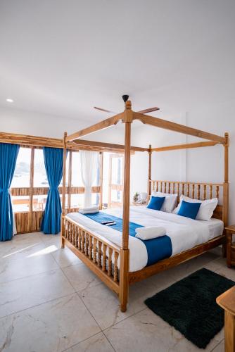 a wooden canopy bed in a bedroom with blue curtains at Dhanrains La Rocha in Patnem