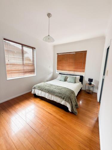 a white bedroom with a bed and a wooden floor at Sweet Home in Avalon in Lower Hutt