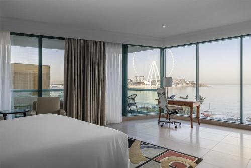 a hotel room with a bed and a desk and windows at Hilton Dubai Jumeirah in Dubai