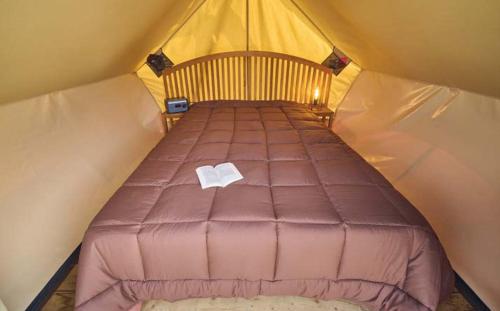 a bed in a tent with a book on it at Camping Valencia el Saler in El Saler