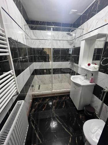 a black and white bathroom with a shower and a sink at Apartamentele Liliacul in Sighetu Marmaţiei