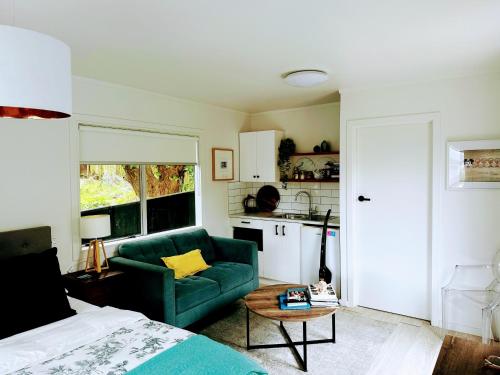 a living room with a green couch and a kitchen at Private Beachside Studio with Courtyard and Sea view in Paraparaumu