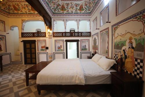 a bedroom with a large bed with paintings on the walls at Haveli Kesar Vilas in Chāran ki Dhāni