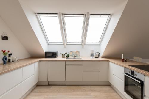 an attic kitchen with white cabinets and windows at Sunlit Loft Apartment in Valby with Parking for 8 in Copenhagen