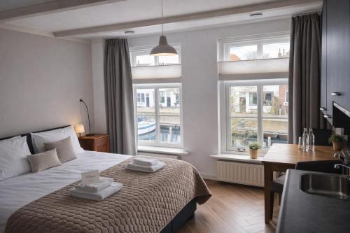 a bedroom with a bed and a desk and two windows at Boutique Hotel De Grote Kade in Goes