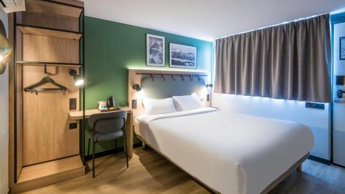 a bedroom with a large white bed and a desk at Campanile NATURE - Strasbourg Sud Geispolsheim in Geispolsheim