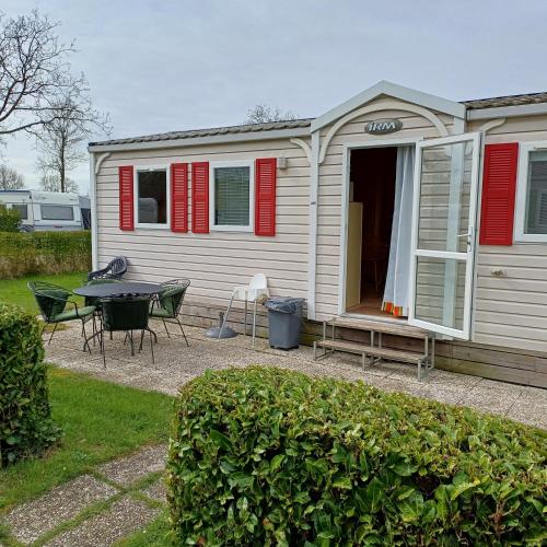a house with red shutters and a table in a yard at Mobilhome 3 slaapkamers Ardoercamping Landingsweg 1 in Baarland