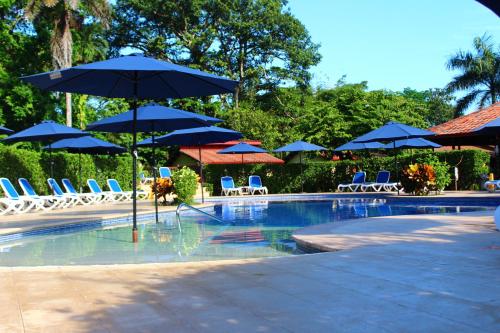 a swimming pool with blue umbrellas and chairs and tables at La Foresta Nature Resort in Quepos