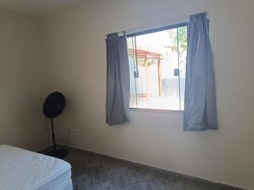 a bedroom with a window with blue curtains and a fan at Suíte Externa Casal in Rio das Ostras