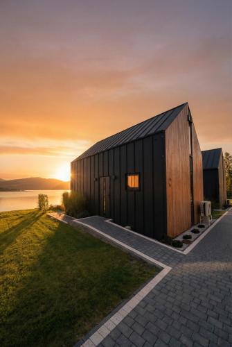 a black building with a sunset in the background at Muchatki domki z sauną in Zagórze