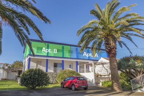 a red car parked in front of a building with a palm tree at Porto Martins Bay Apartments (AL) in Porto Martins
