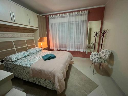 a bedroom with a bed and a chair and a window at AP perto do HSVP com estacionamento in Passo Fundo