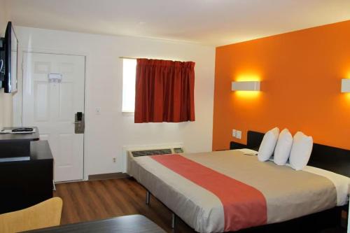a hotel room with a bed with an orange wall at Motel 6 Augusta GA Fort Gordon in Augusta