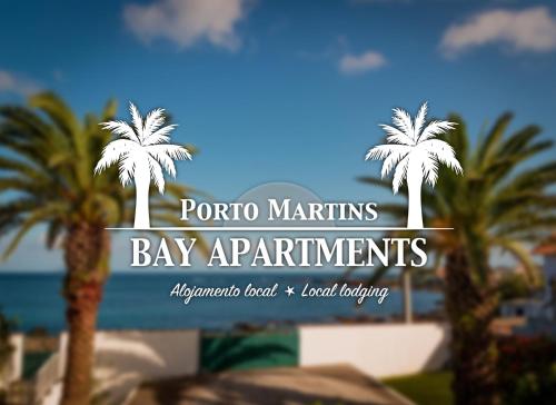 a sign for a bay apartments with palm trees at Porto Martins Bay Apartments (AL) in Porto Martins