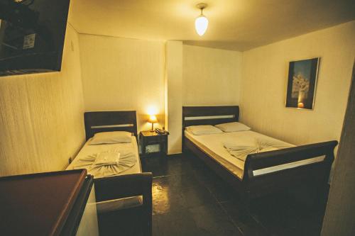 two beds in a small room with two tables at Hotel Pousada Del Rey in Macaé