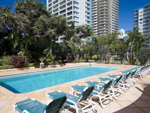 a swimming pool with lounge chairs and trees and buildings at BreakFree Beachpoint in Gold Coast