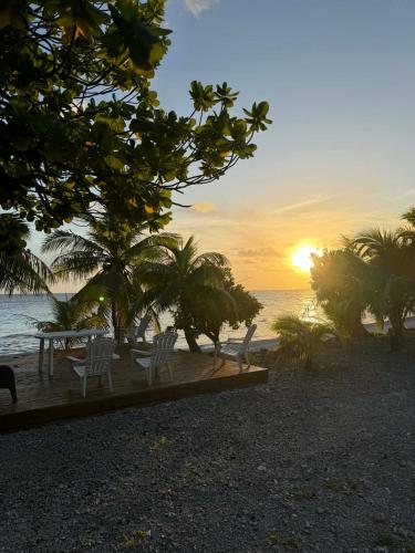 a sunset on a beach with chairs and palm trees at MONITA VILLA Rangiroa in Tiputa