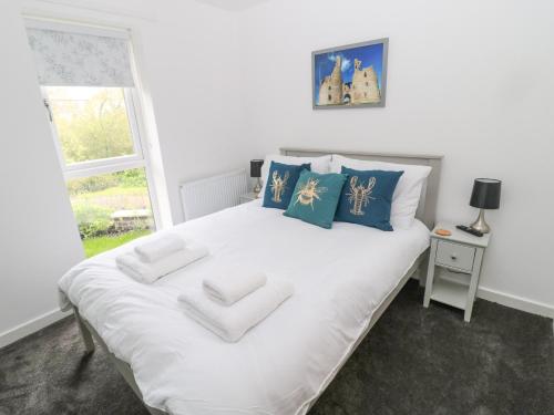 a white bed with blue pillows and a window at Summer Rose in Craster