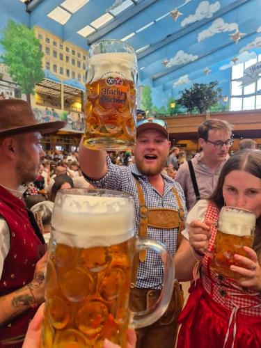 a man holding up two large glasses of beer at Beer Base-Camp Oktoberfest camping with free welcome beer and traditional dirndl-lederhosen shop in Munich