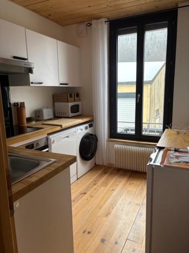 una cucina con mobili bianchi e pavimenti in legno e una finestra di Superbe appartement a Le Mont-Dore