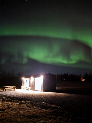 a cabin under the aurora in a field with a bench at Sóltún -A cozy modern cabin in Klettaholt by the Golden Circle in Blaskogabyggo