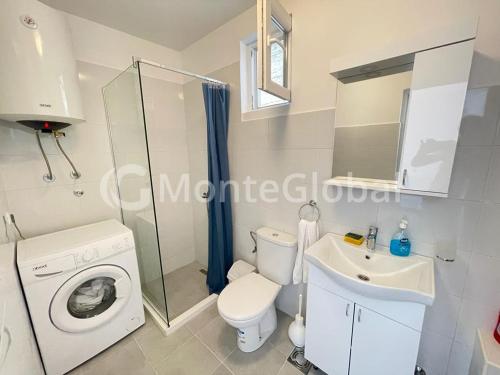 a bathroom with a toilet a sink and a washing machine at Apartmans White perl in Sutomore