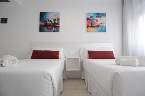 two beds in a white room with paintings on the wall at Hotel Gabriel y Galán in Salamanca