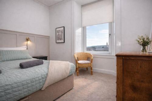 a bedroom with a bed and a chair and a window at Portside Apartment in Greenock