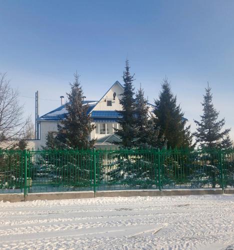 a fence in front of a house with trees at Усадьба in Kostanay