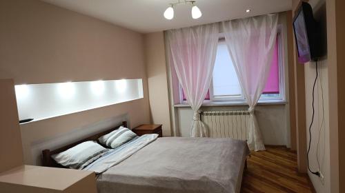 a bedroom with a bed and a window with pink curtains at Home for you in Ternopil