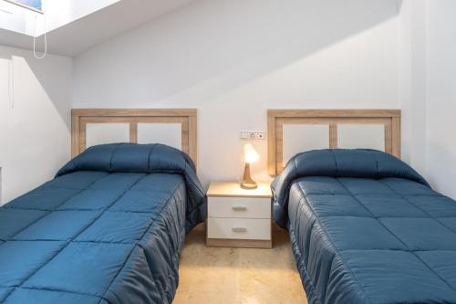 two beds in a room with blue comforters and a lamp at Villa Rural Las Lomas in Jaén