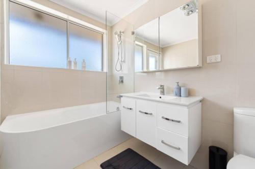 a bathroom with a sink and a tub and a mirror at Comfortable Home for 6 - Canberra Inner North in Belconnen