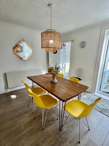 a dining room with a wooden table and yellow chairs at Sea Song Cottage in Broadstairs