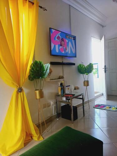 ein Wohnzimmer mit einem gelben Vorhang und einem Fernseher in der Unterkunft Résidence Meublée Pachira I in Abidjan