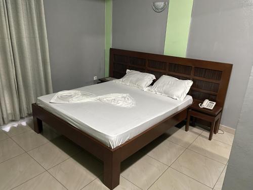 un letto con lenzuola bianche e una testiera in legno di Ngueye Hotel a Yaoundé