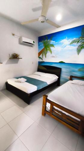 two beds in a room with a painting of the ocean at frente al mar Hotel La Morena in Taganga