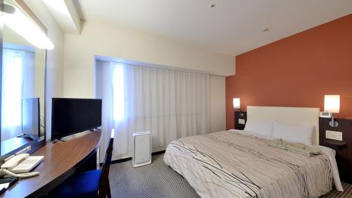 a bedroom with a bed and a desk with a television at Takaoka Manten Hotel Ekimae in Takaoka