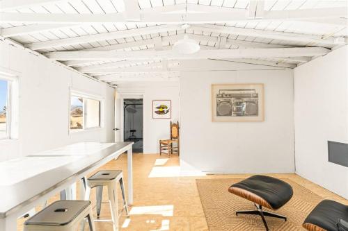 a white living room with a counter and stools at The Sawtooth House - Pioneertown Escape with Pool, Spa, Views & Fire Pit in Pioneertown