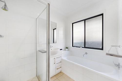 a white bathroom with a tub and a sink at 4BR Family Home Coomera Theme Parks Shopping in Gold Coast