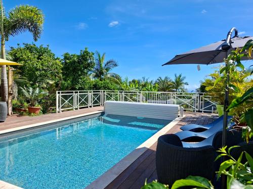 a swimming pool with an umbrella and chairs next to a house at Le Palmier de la Paix in Le Tampon