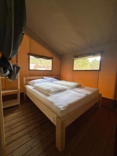 a bed in a small room with two windows at Glampingtent Serengeti in Zwartemeer