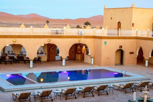 a large swimming pool in a building with chairs around it at Hotel Sunset Palace Merzouga in Merzouga
