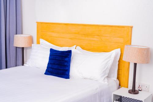 a white bed with a wooden headboard and a blue pillow at 7th Heaven Apartments in Gaborone