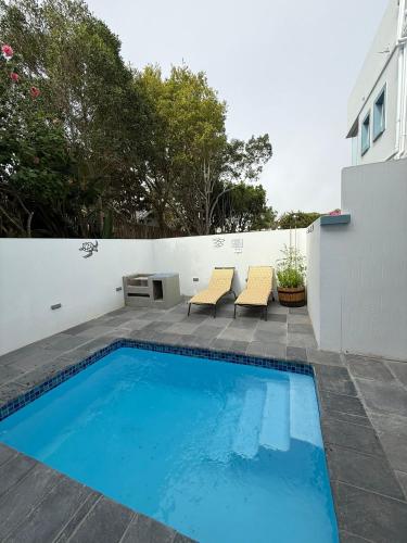 a swimming pool with two chairs next to a white wall at Ocean Whisper in Plettenberg Bay