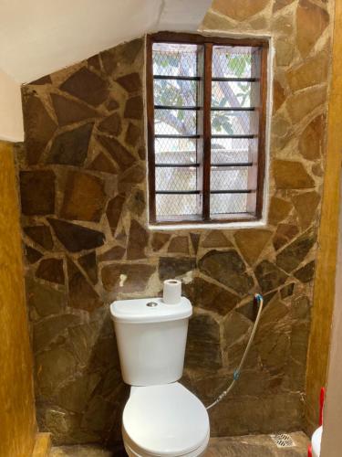 a bathroom with a toilet and a stone wall at Petcat Cottage in Diani Beach
