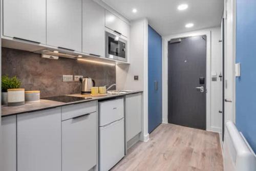 a kitchen with white cabinets and a blue wall at Practical Studios In Lincoln with Free Grab&Go Breakfast in Lincoln
