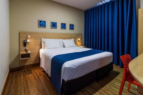 a bedroom with a large bed with blue curtains at Luds Comfort Hotel in Ponta Grossa