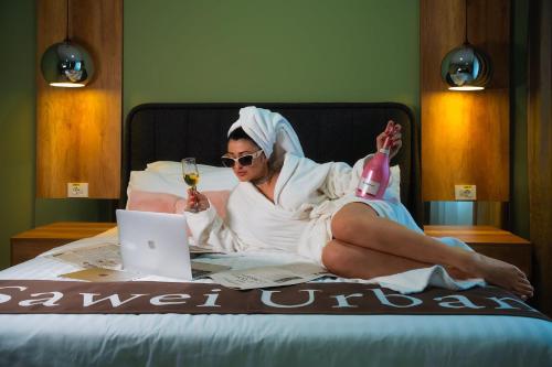 a woman laying on a bed with a glass of wine and a laptop at Sawei Urban Hotel in Craiova