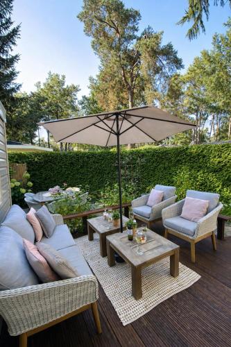 a patio with couches and a table with an umbrella at Luxe Chalet met prachtig terras op de Veluwe , veel privacy in Hoenderloo