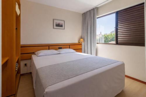 a bedroom with a large bed and a window at Hotel Flat Petras Residence in Curitiba